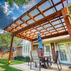 Wooden pergola with a clear skypoly cover protecting a patio with furniture. 